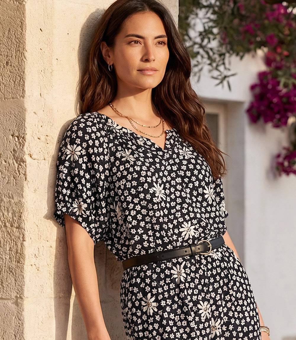 Woman wearing a black and white floral dress against a stone wall with flowers.