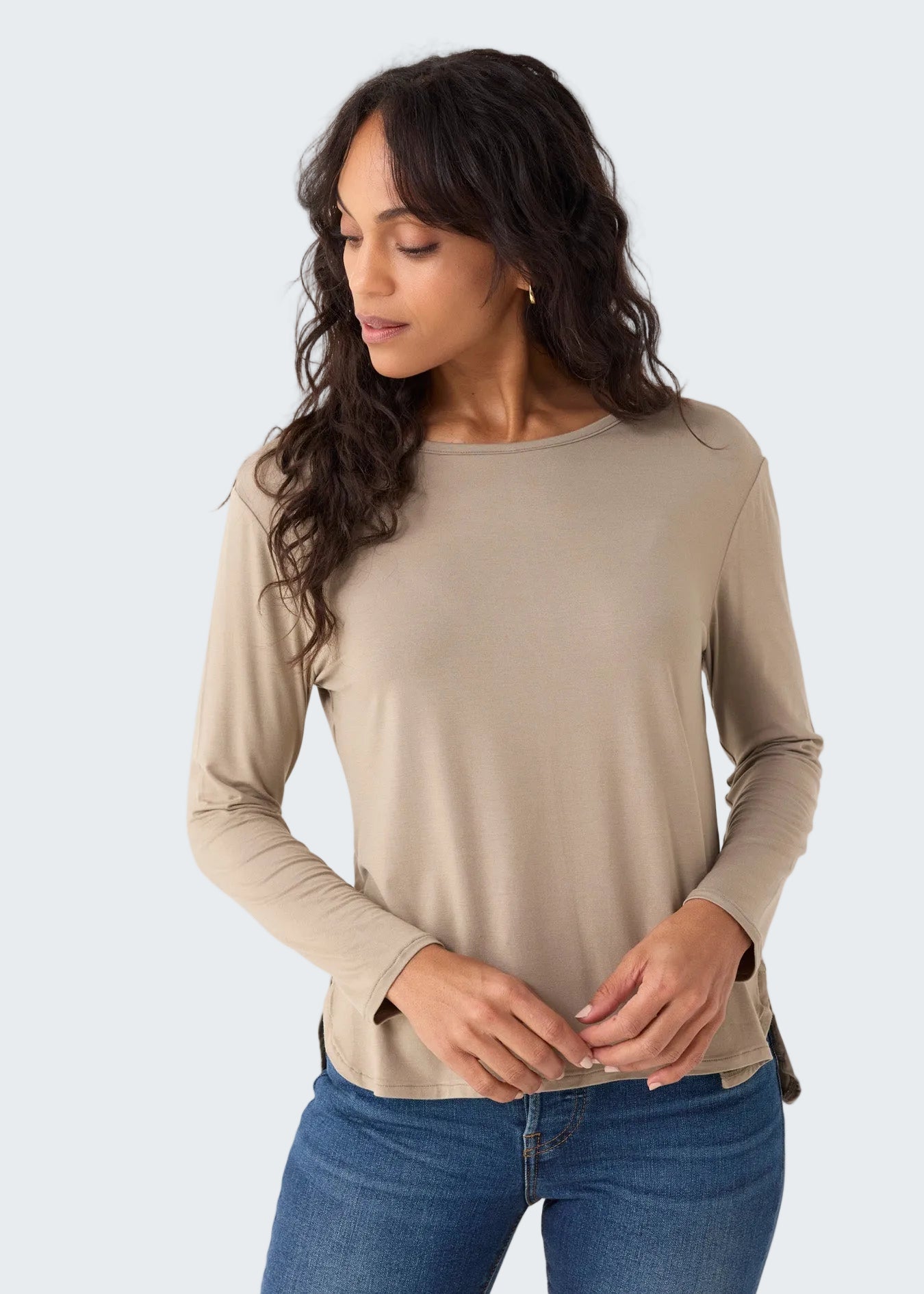 Woman wearing a beige long-sleeve top and blue jeans on a white background