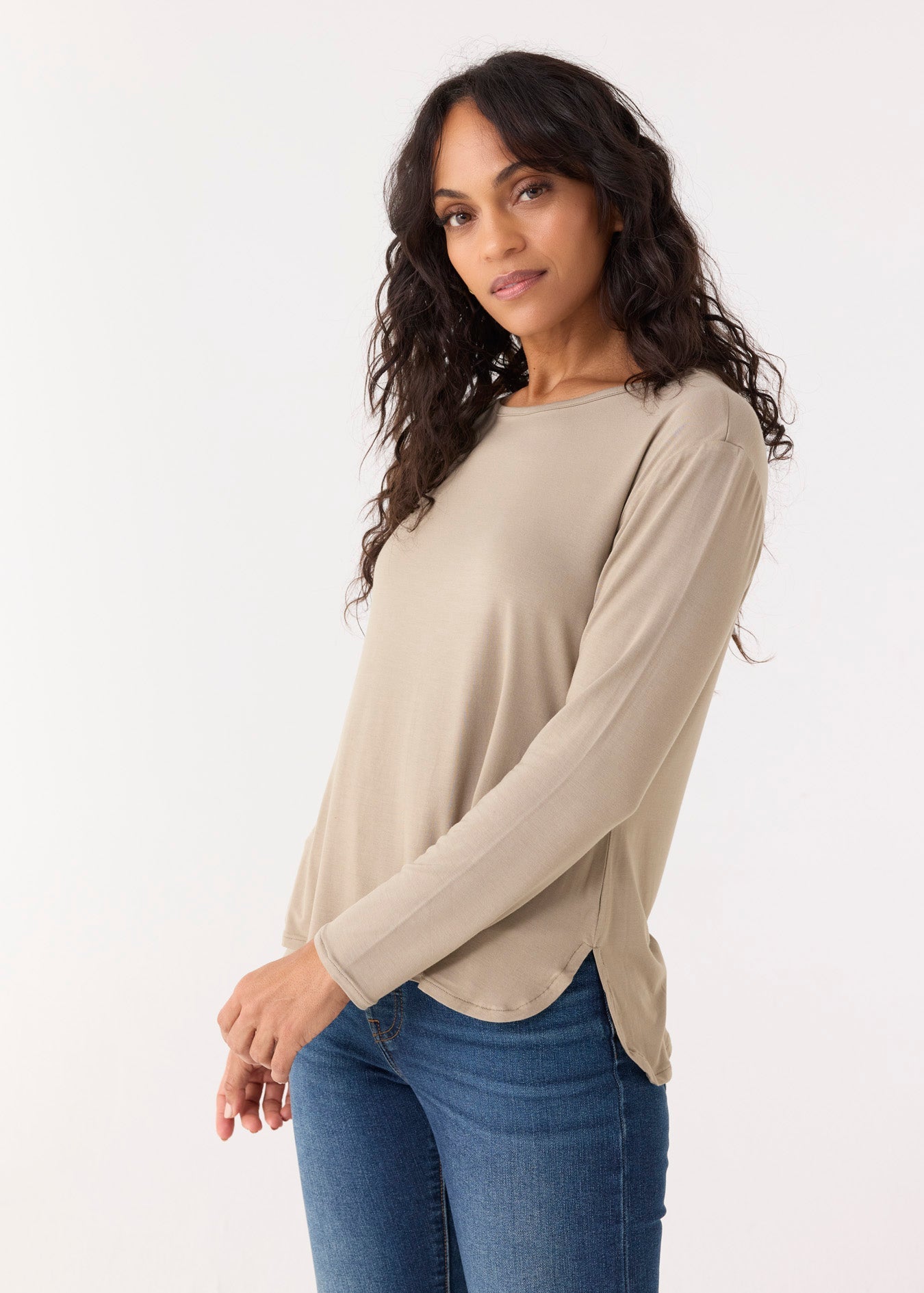 Woman wearing a beige long-sleeve top and blue jeans on a white background