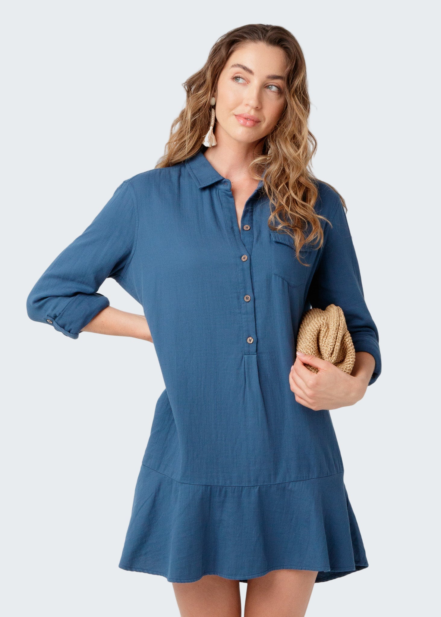 Woman wearing a blue dress holding a clutch against a white background