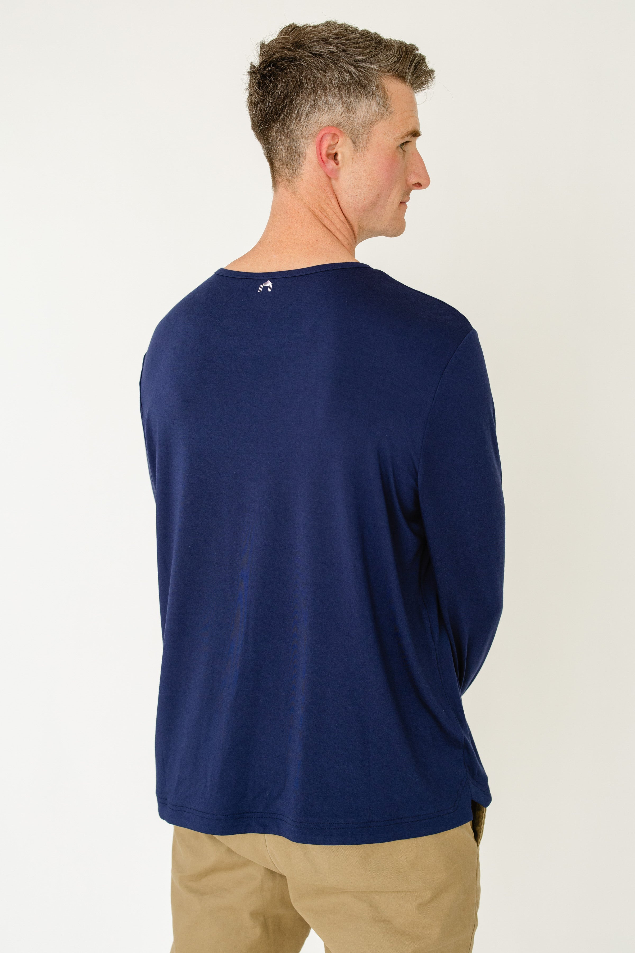 Man wearing a blue long-sleeve shirt with a logo on the back, standing against a white background.