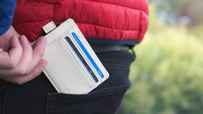 Person holding a beige cardholder with blue accents, wearing a red jacket outdoors.