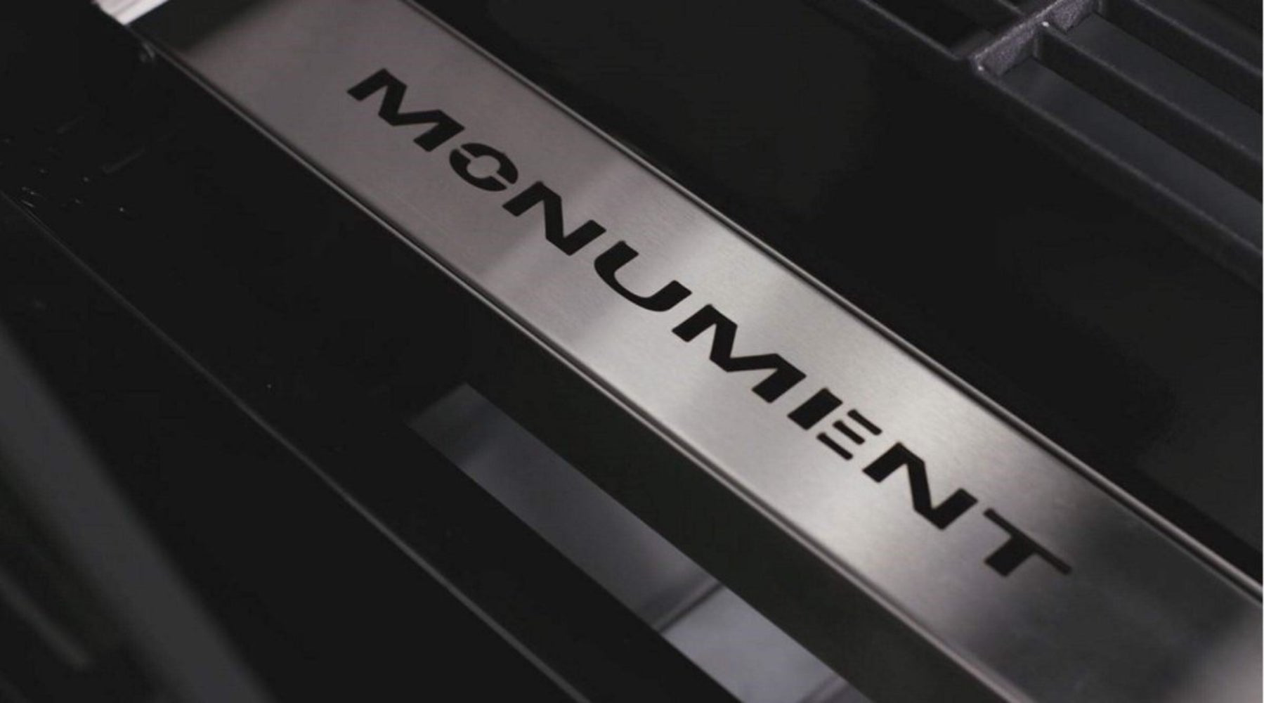 Close-up of a metallic 'MONUMENT' logo on a black background