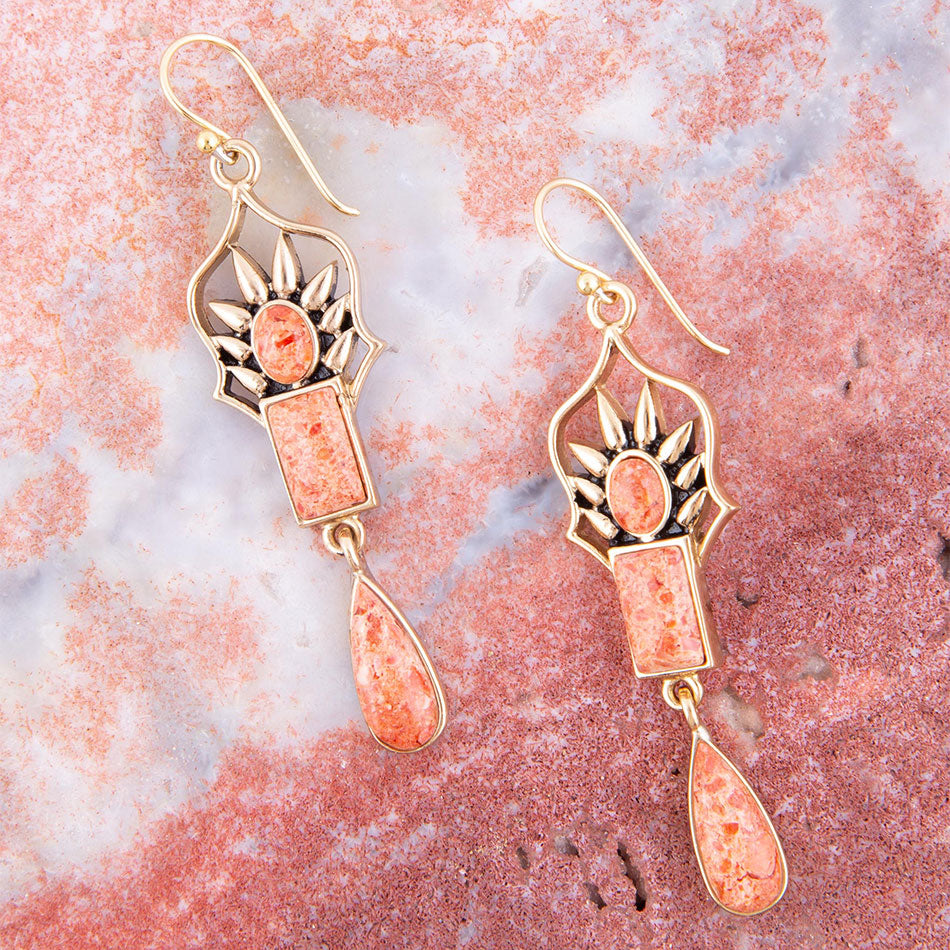 Pair of gold and pink earrings on a pink marble background