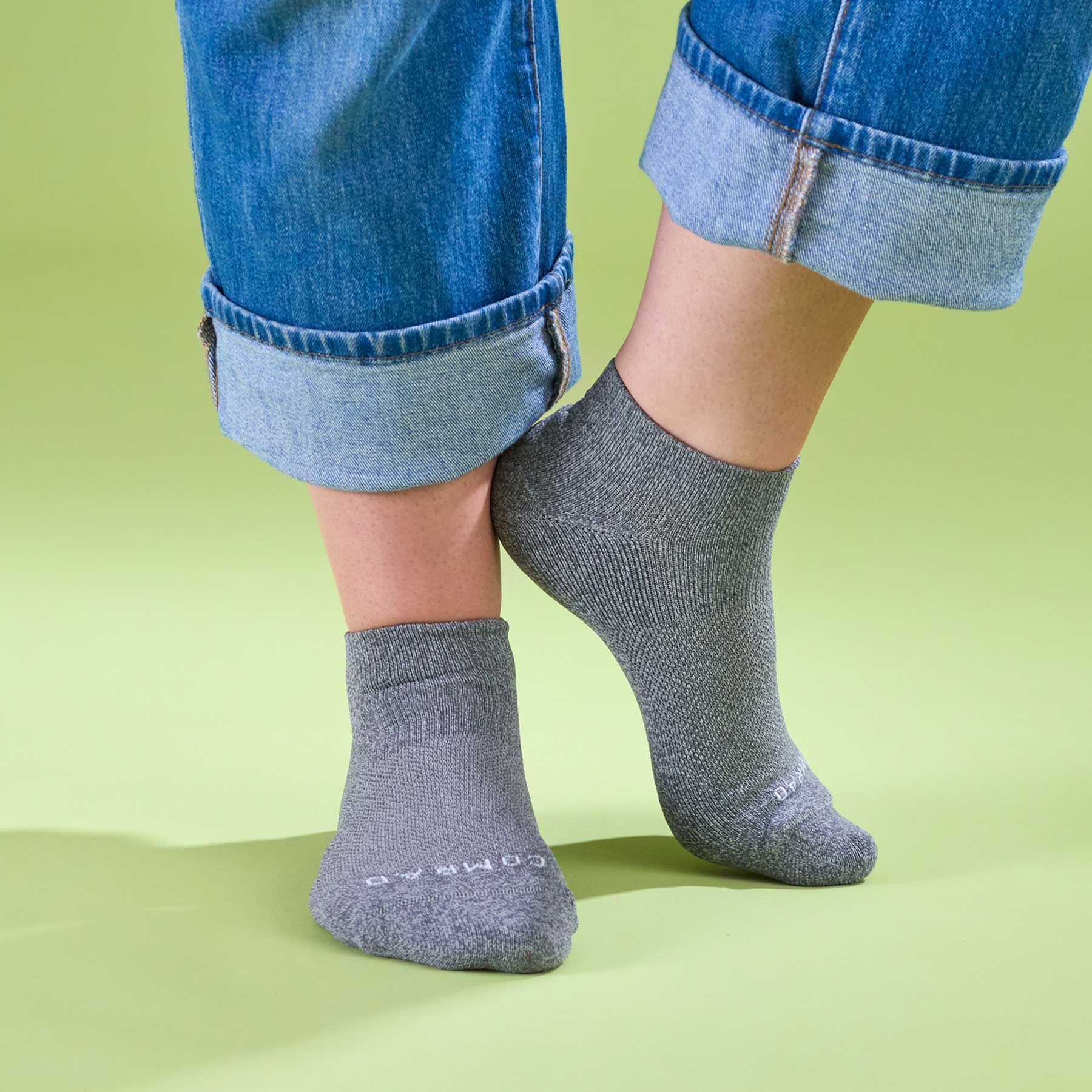 Gray socks worn with rolled-up blue jeans on a green background