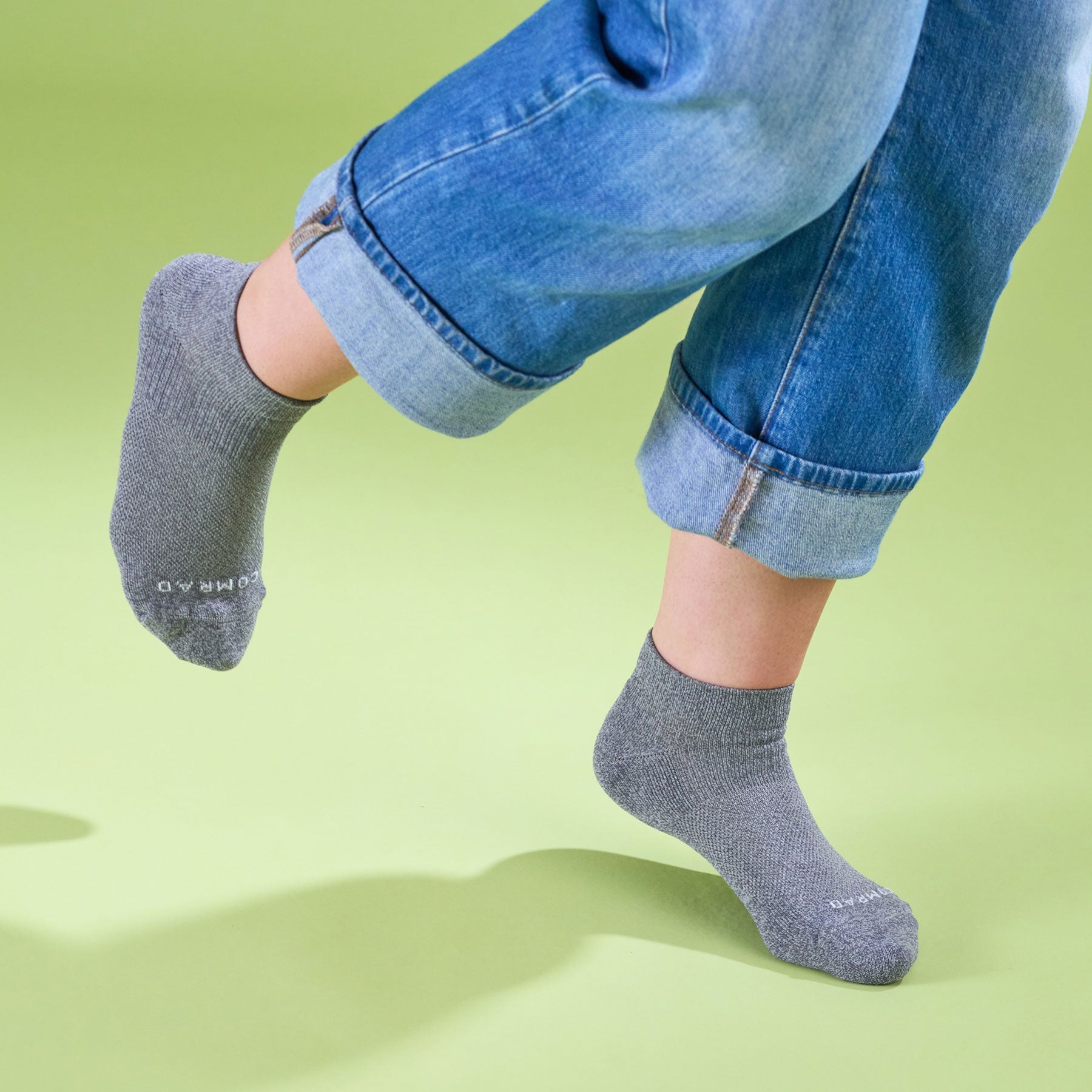 Person wearing gray socks with a brand logo on a green background