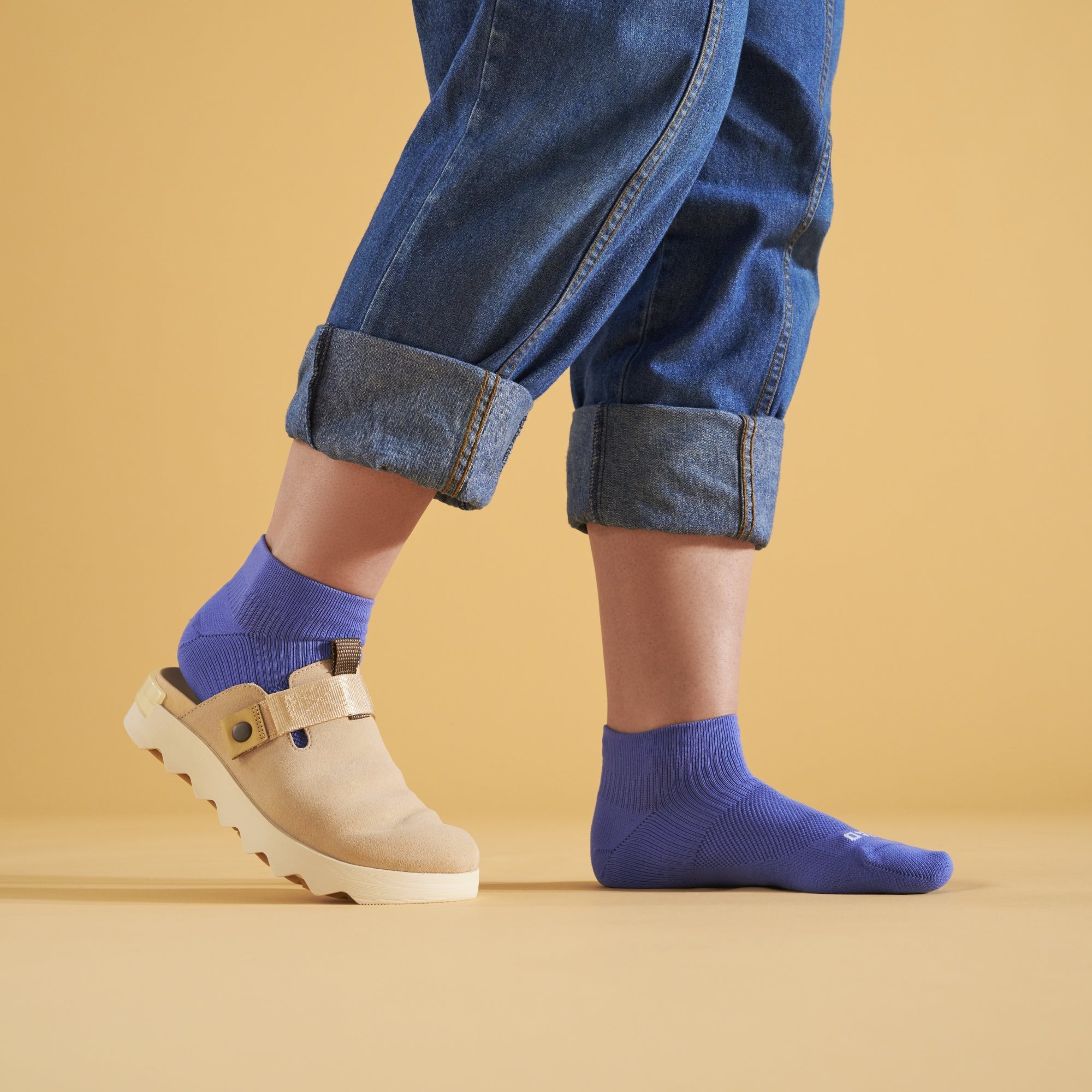 Person wearing blue socks and beige shoes on a yellow background
