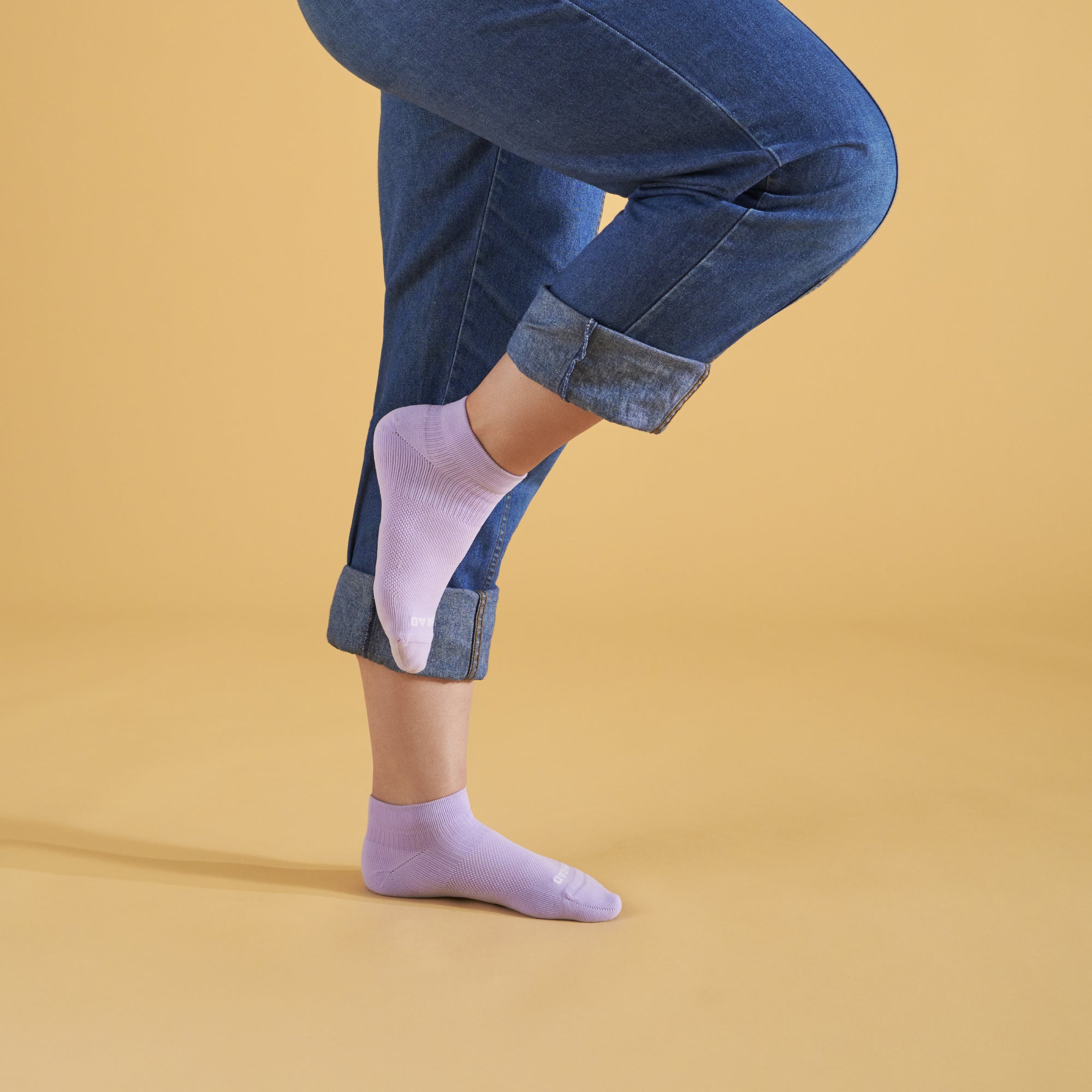 Person wearing light purple socks with rolled-up blue jeans on a beige background
