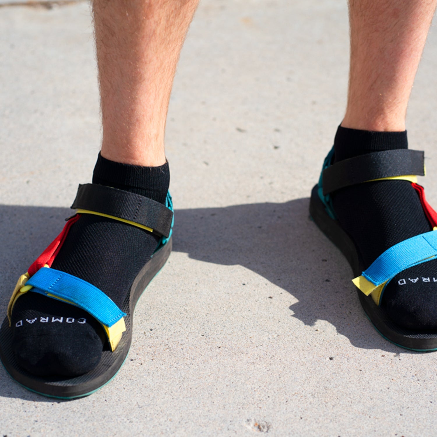 Black sandals with colorful straps worn by a person on a concrete surface