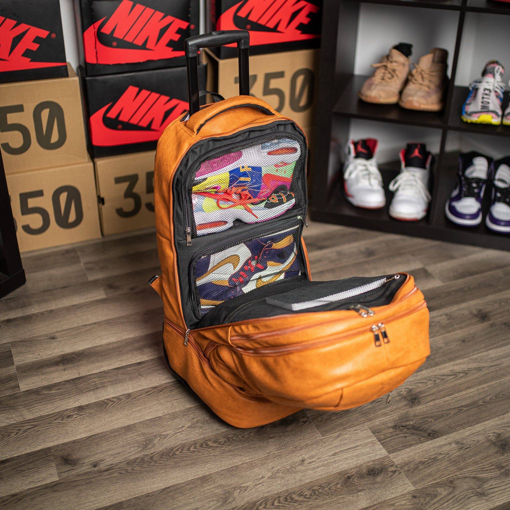 Orange backpack with shoe compartments on a wooden floor with Nike boxes and shoes in the background.