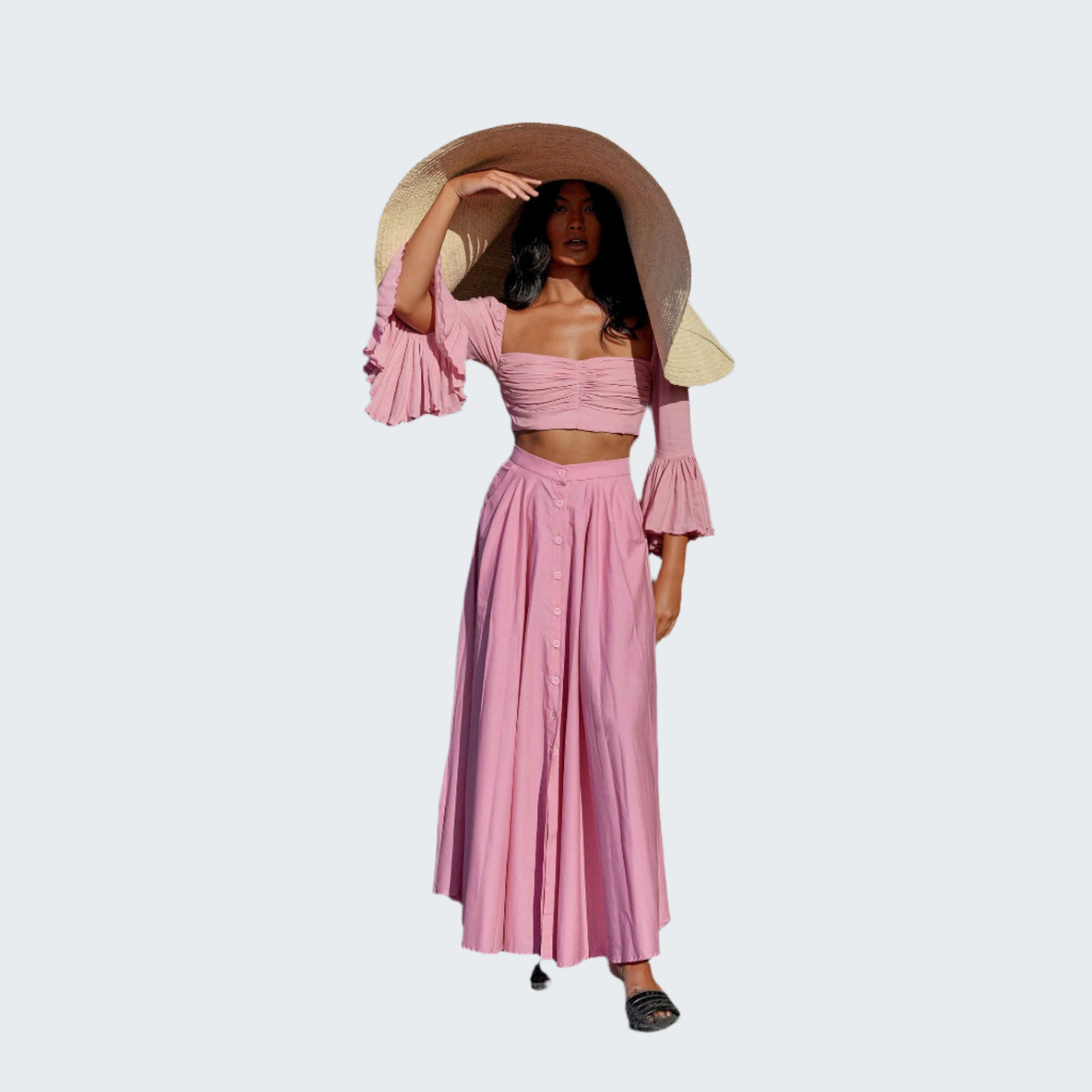 Woman in a pink outfit with a wide-brimmed hat standing in front of green plants.