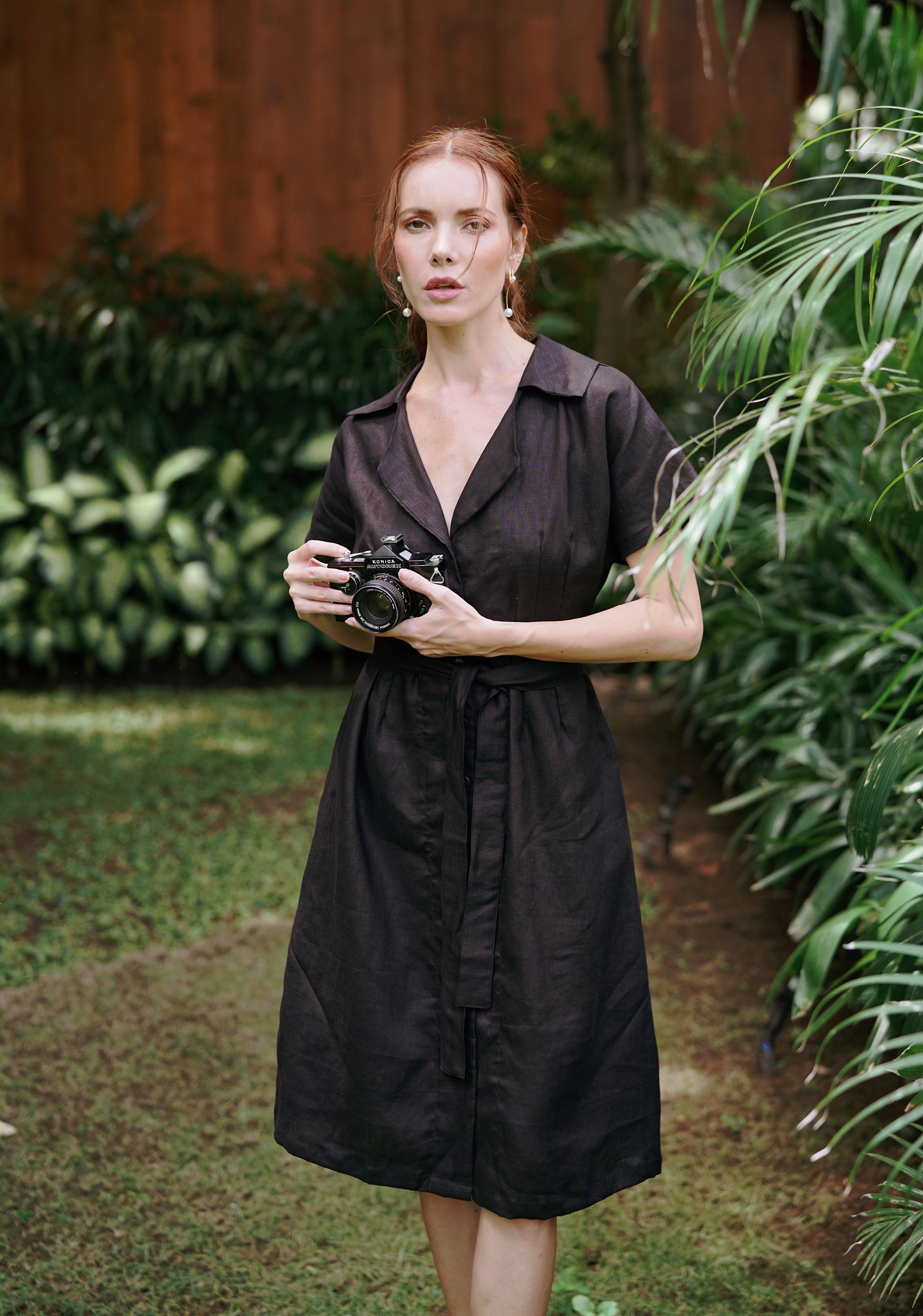 Woman in a black dress holding a camera in a garden setting
