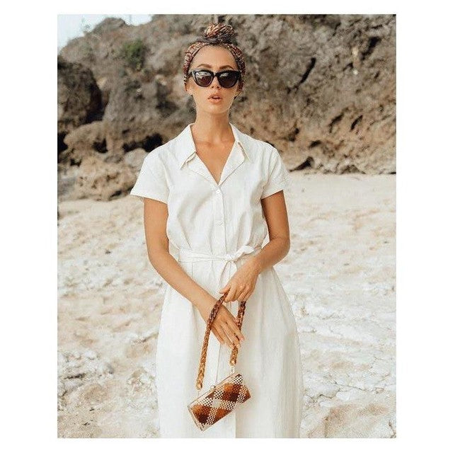 Woman in a white dress holding a handbag on a rocky beach