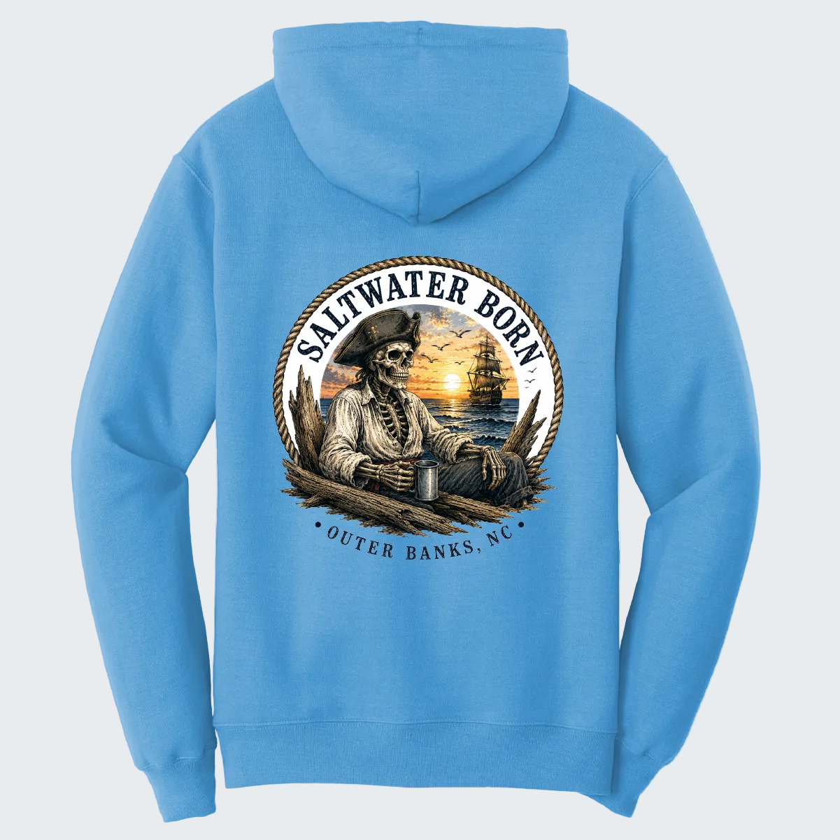 A light blue hoodie shown from the back, featuring a large circular graphic print of a pirate sitting by a sunset on a boat, with the text 'SALTWATER BORN' and 'OUTER BANKS, NC'.