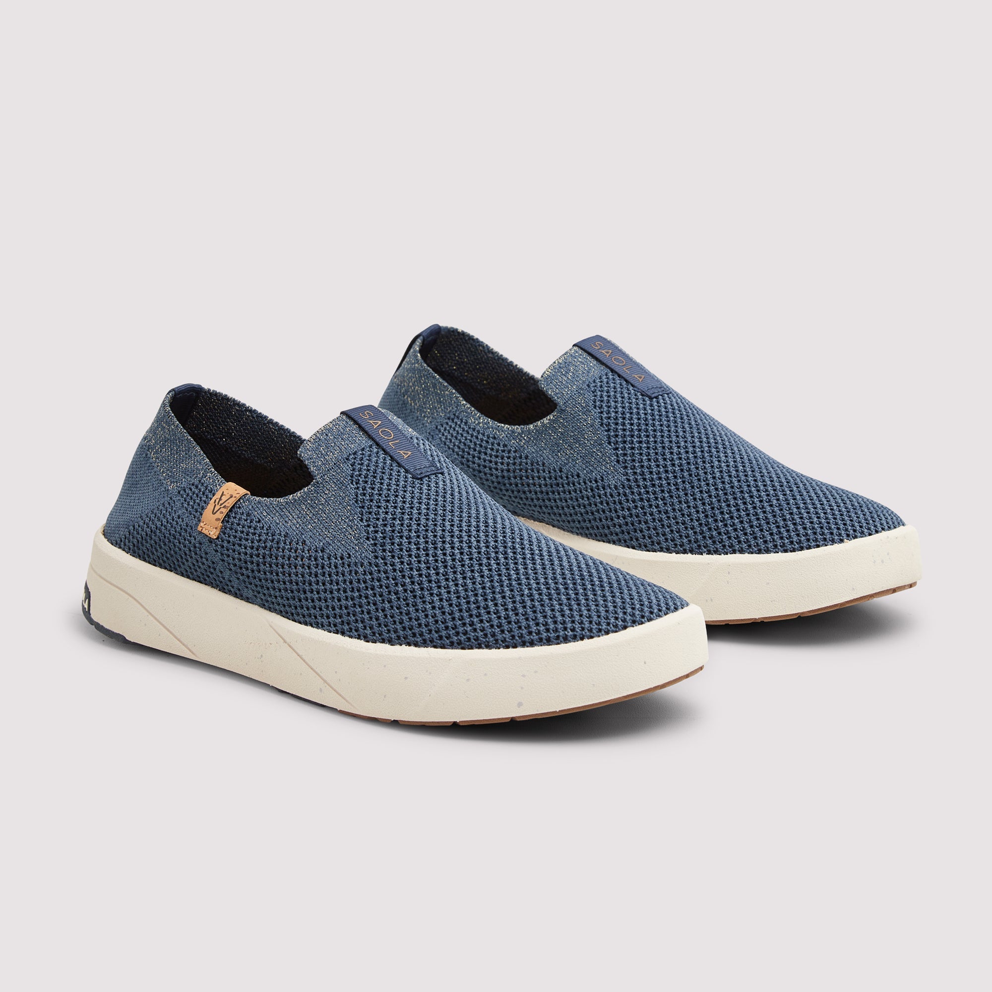 A pair of slip-on sneakers in a textured blue fabric with thick cream-colored soles, displayed on a light gray background.