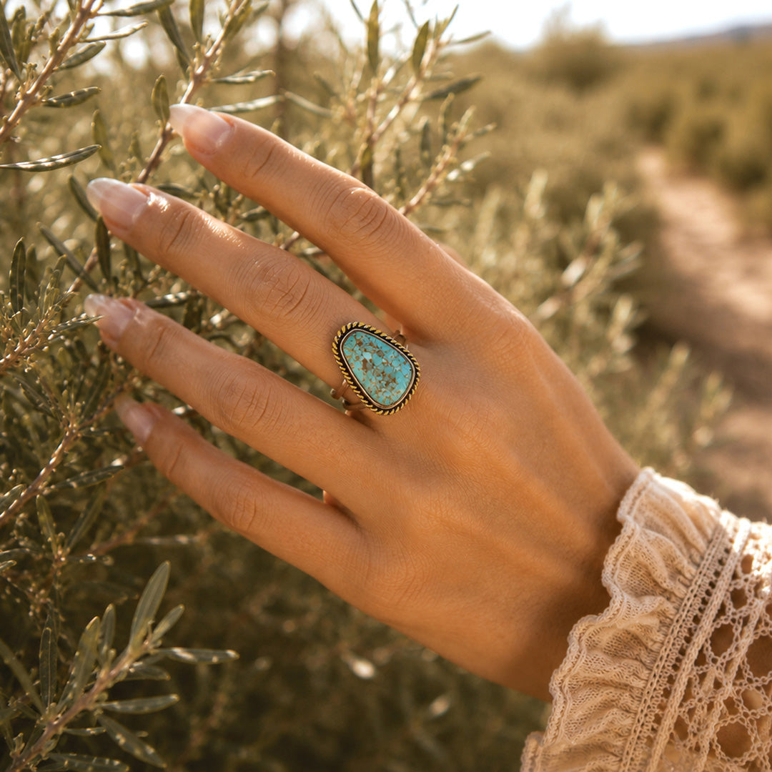 Hand wearing a turquoise ring with a blurred natural background