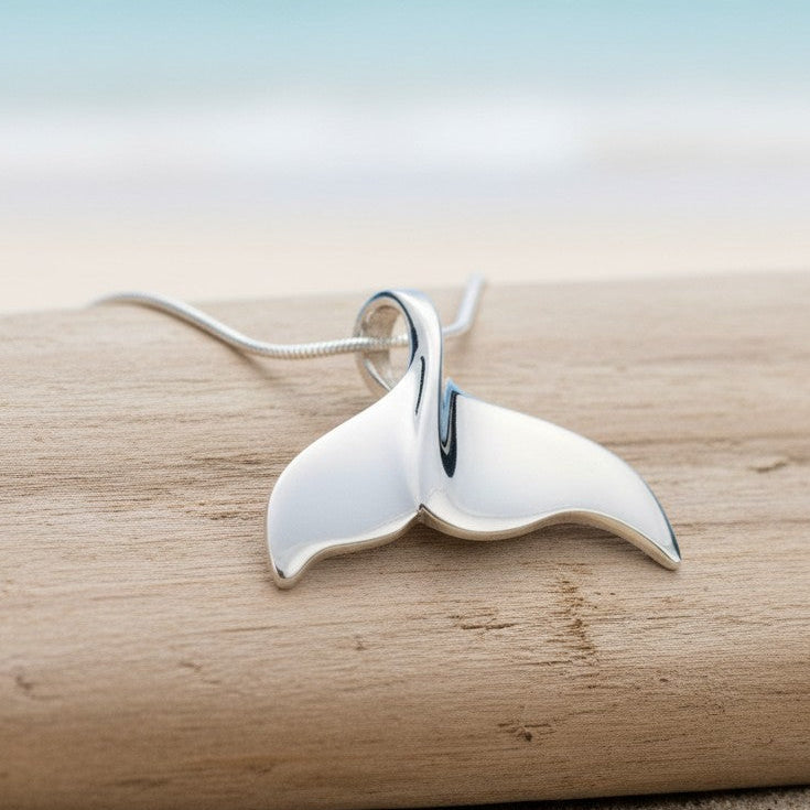 Silver whale tail pendant on a wooden surface with a blurred natural background