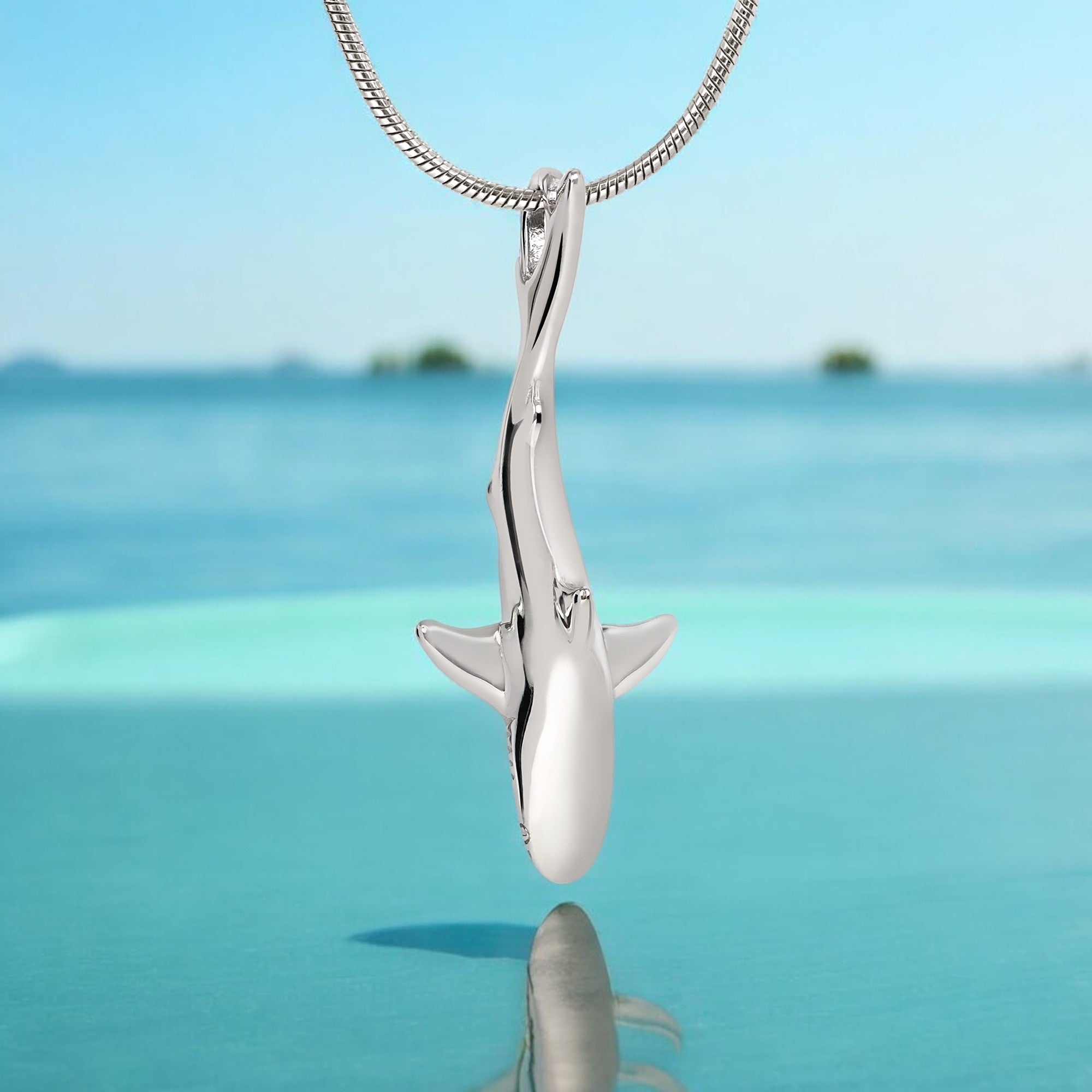 Silver shark pendant on a chain with a blue ocean background