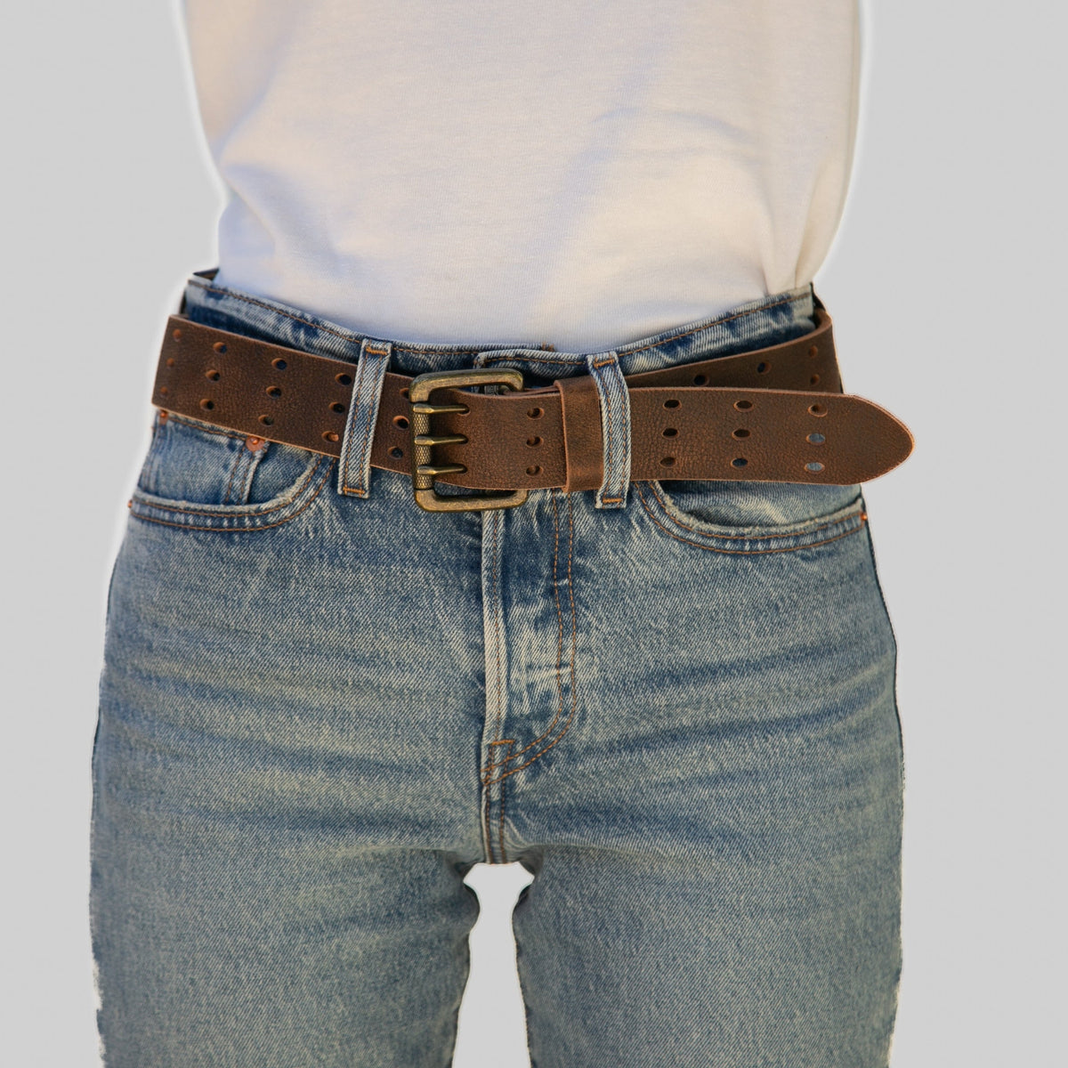 Mannequin wearing blue jeans with a brown belt on a plain background