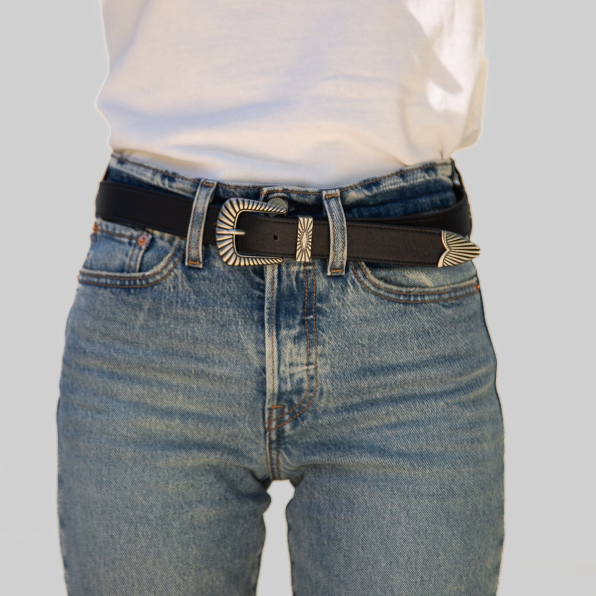 Person wearing blue jeans with a black belt and silver buckle on a light gray background