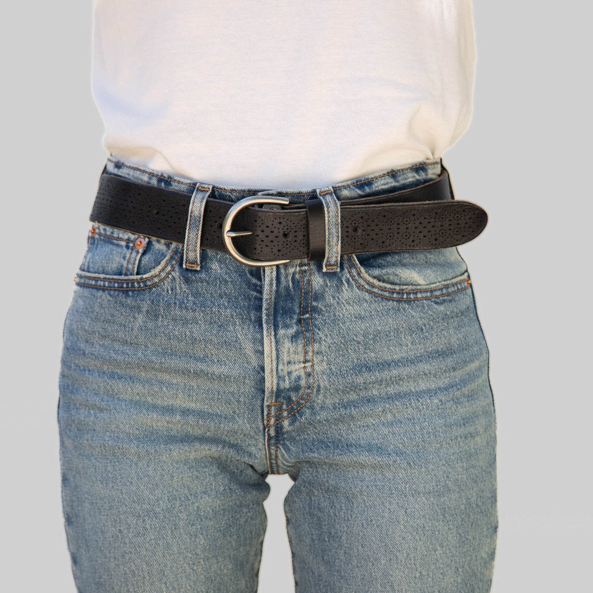 Person wearing blue jeans with a black belt on a light gray background