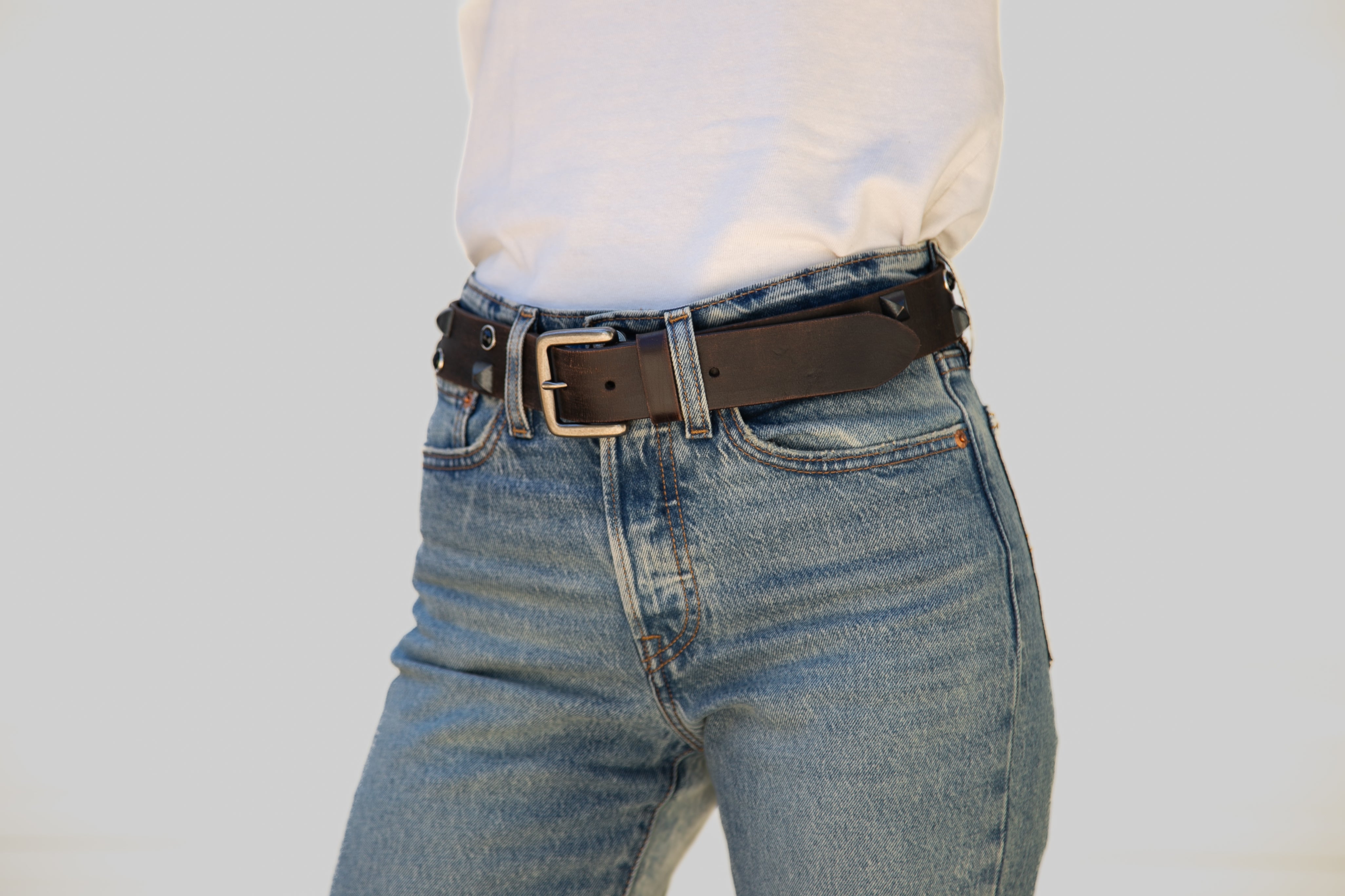 Person wearing blue jeans with a brown belt on a plain background