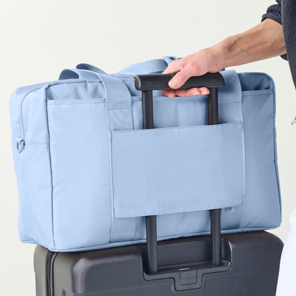 Light blue duffel bag with black handle being held over a suitcase on a light gray background