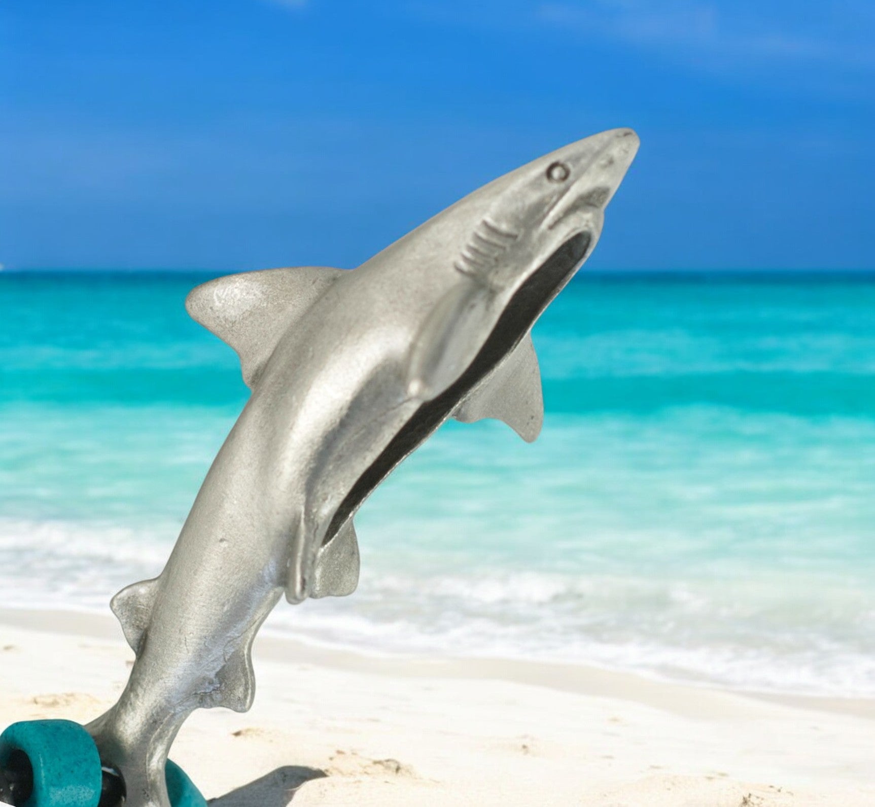 Metallic shark figurine on a sandy beach with turquoise water and blue sky in the background