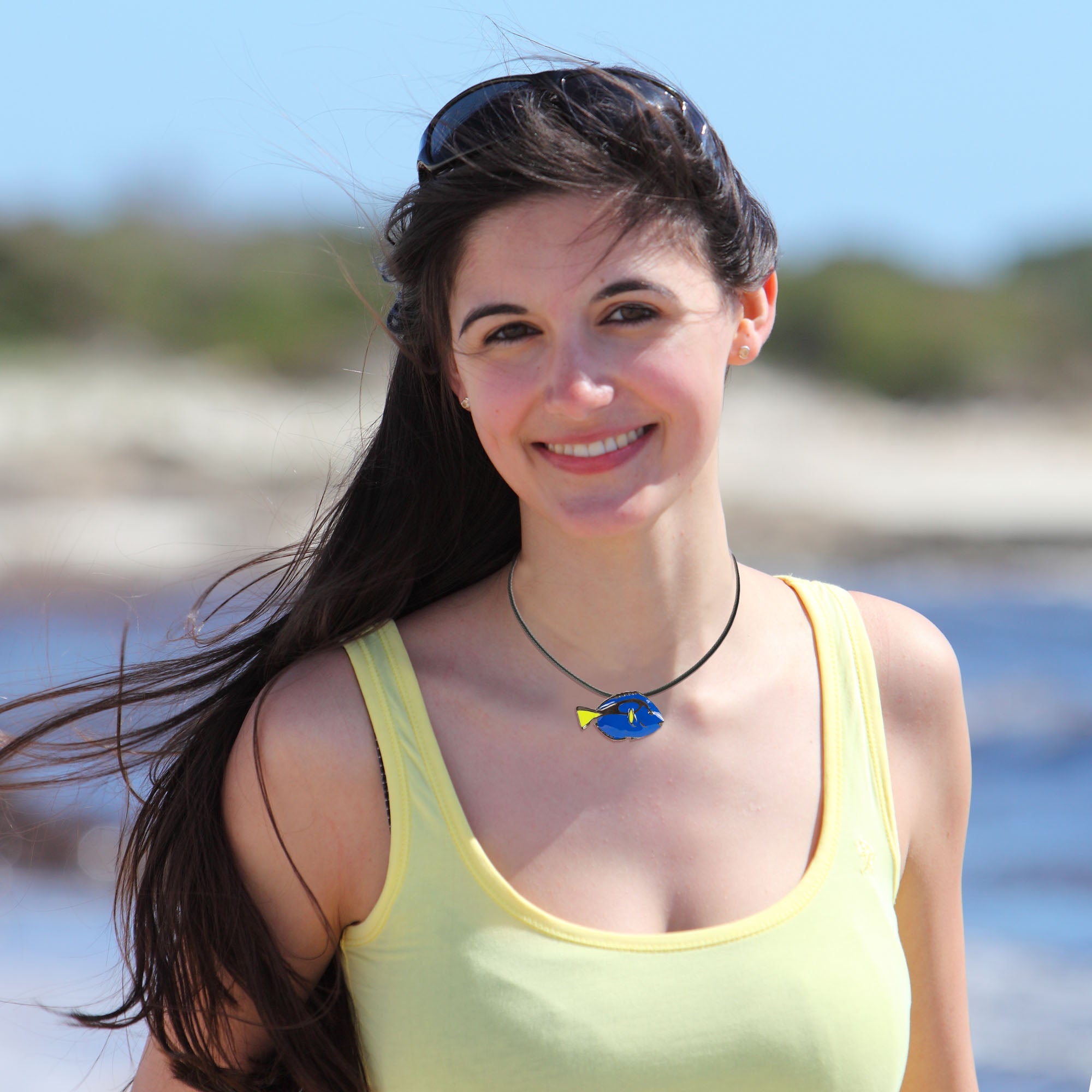 Woman in a yellow tank top with a blue necklace by a body of water