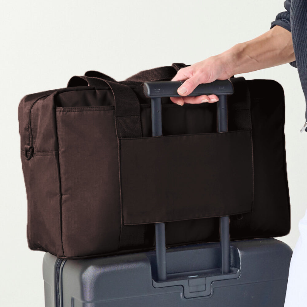 Brown duffel bag with black handle on top of a gray suitcase against a white background