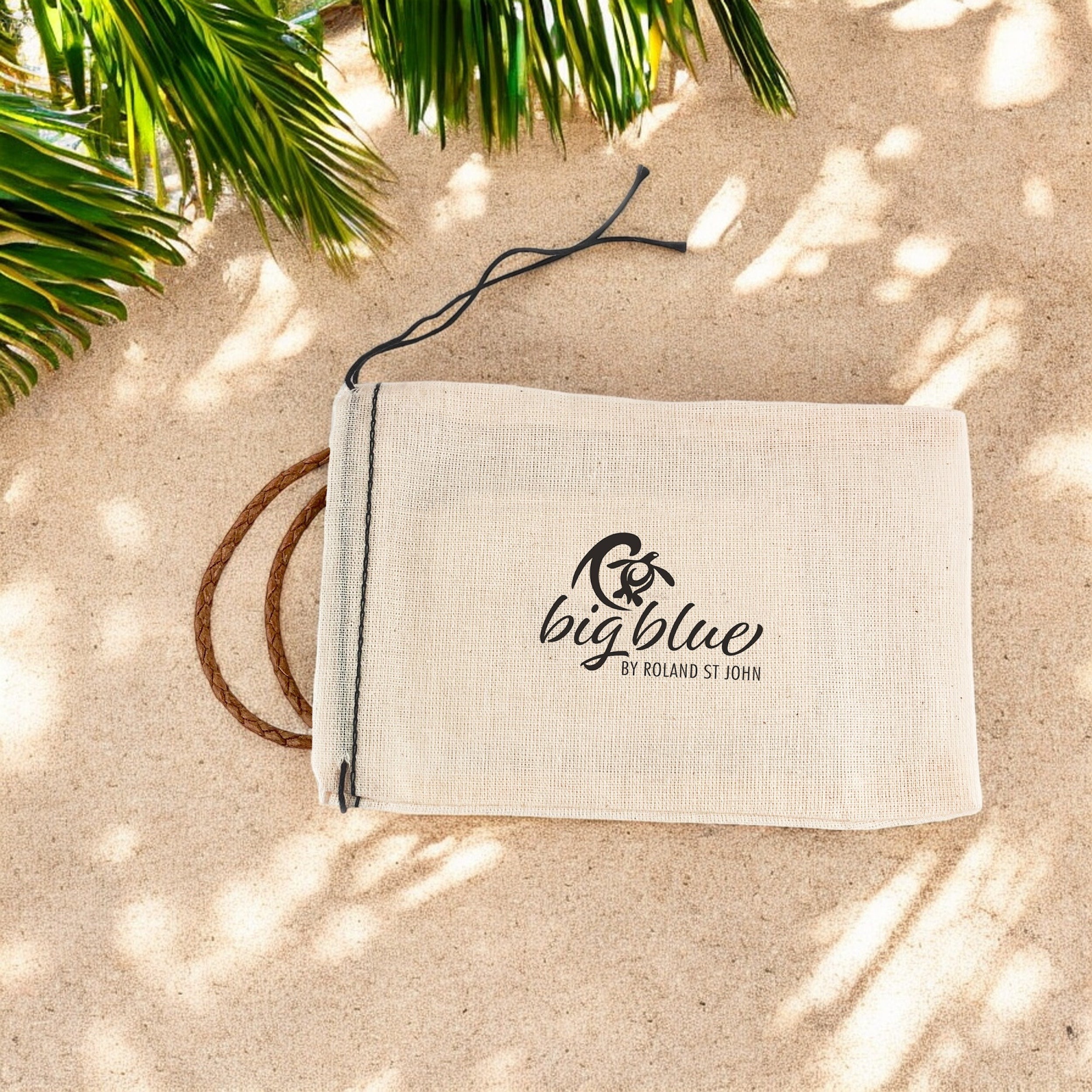 Beige pouch with 'big blue' logo on sand with palm leaves