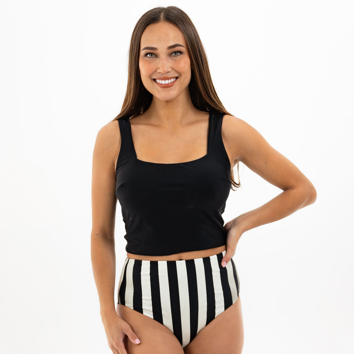 Woman wearing a black tank top and black and white striped high-waisted bikini bottom on a white background
