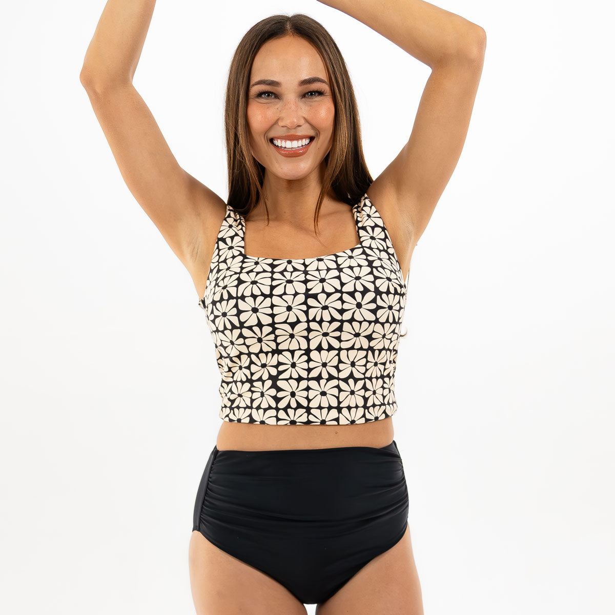 Woman wearing a black and white patterned bikini top and black high-waisted bottoms on a white background