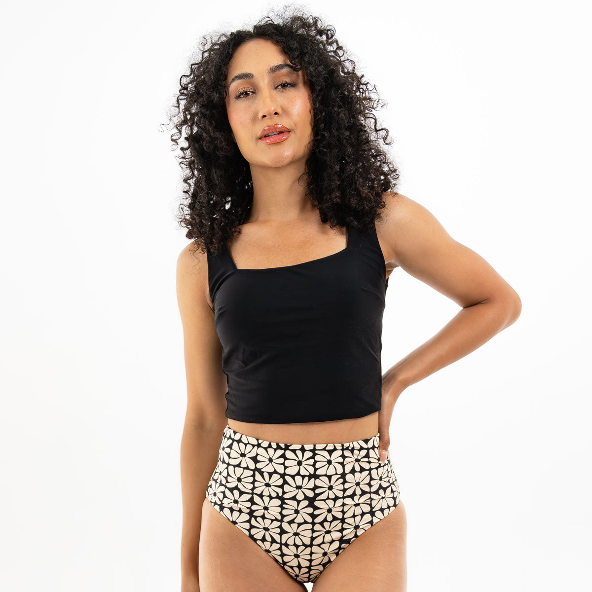 Woman wearing a black tank top and patterned high-waisted shorts on a white background