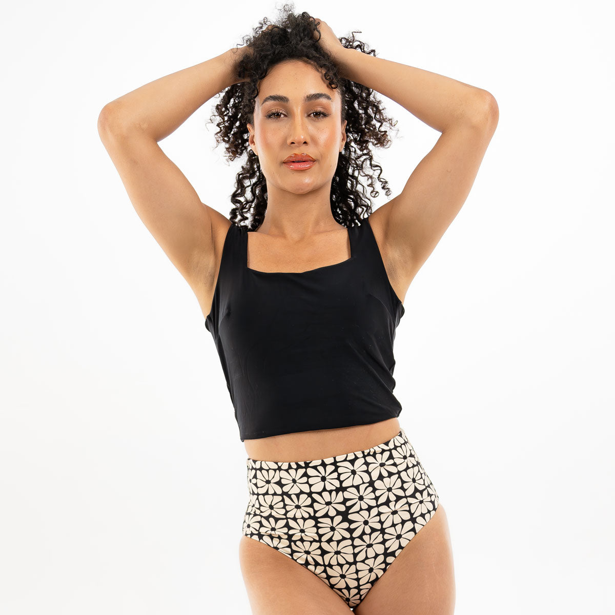 Woman wearing a black tank top and patterned high-waisted shorts on a white background