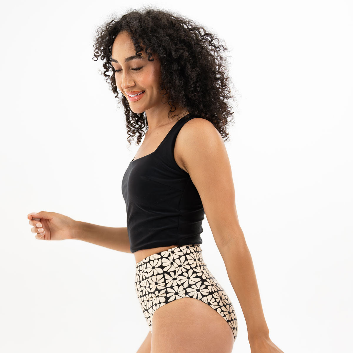 Woman wearing a black tank top and patterned high-waisted shorts on a white background