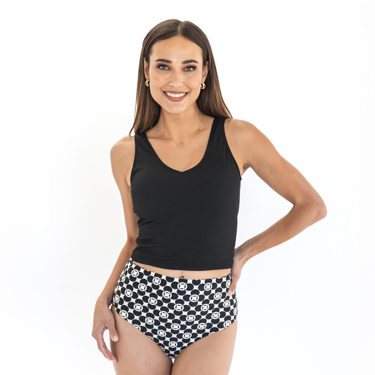 Woman wearing a black tank top and black and white patterned high-waisted bikini bottom on a white background