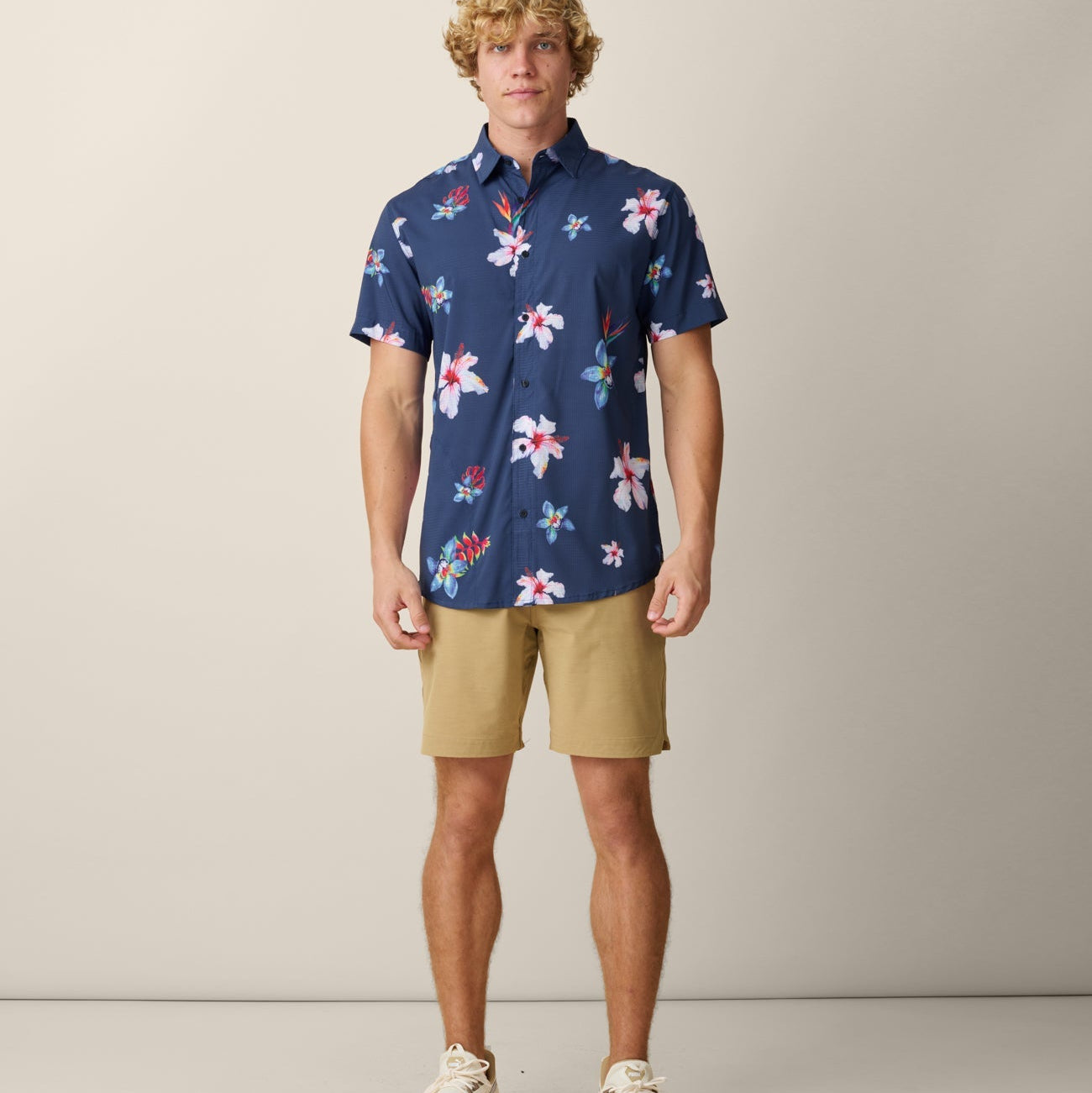 Man wearing a navy floral shirt and beige shorts against a plain background
