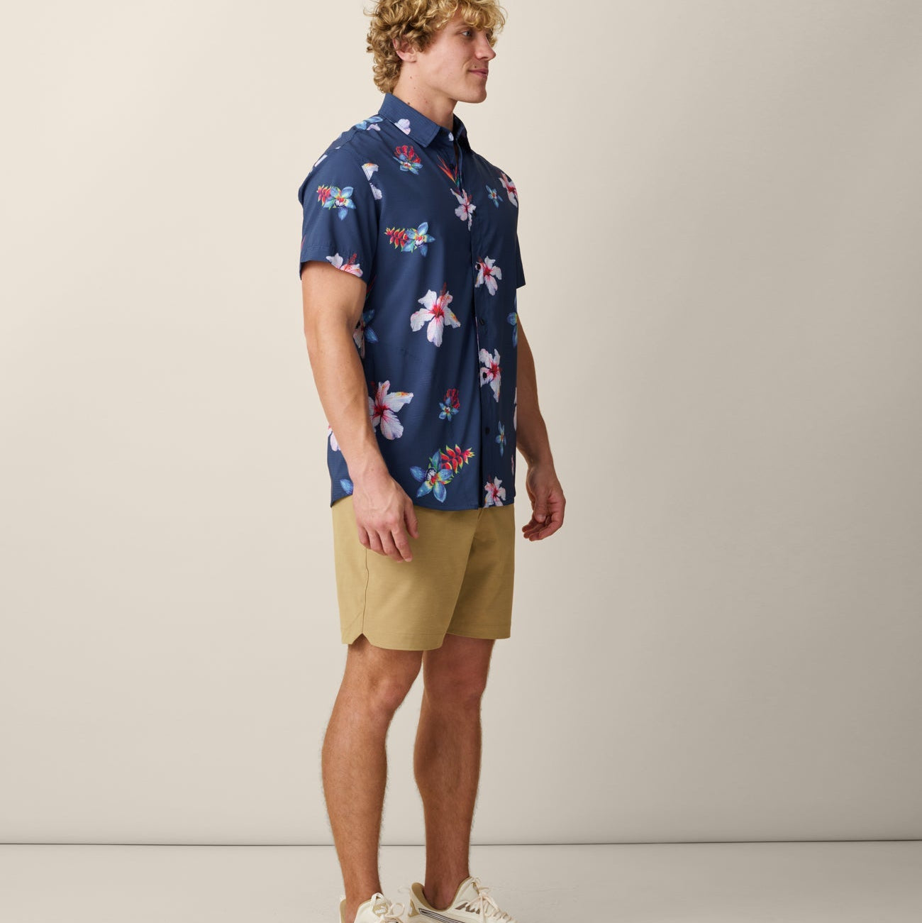 Man wearing a blue floral shirt and beige shorts on a plain background