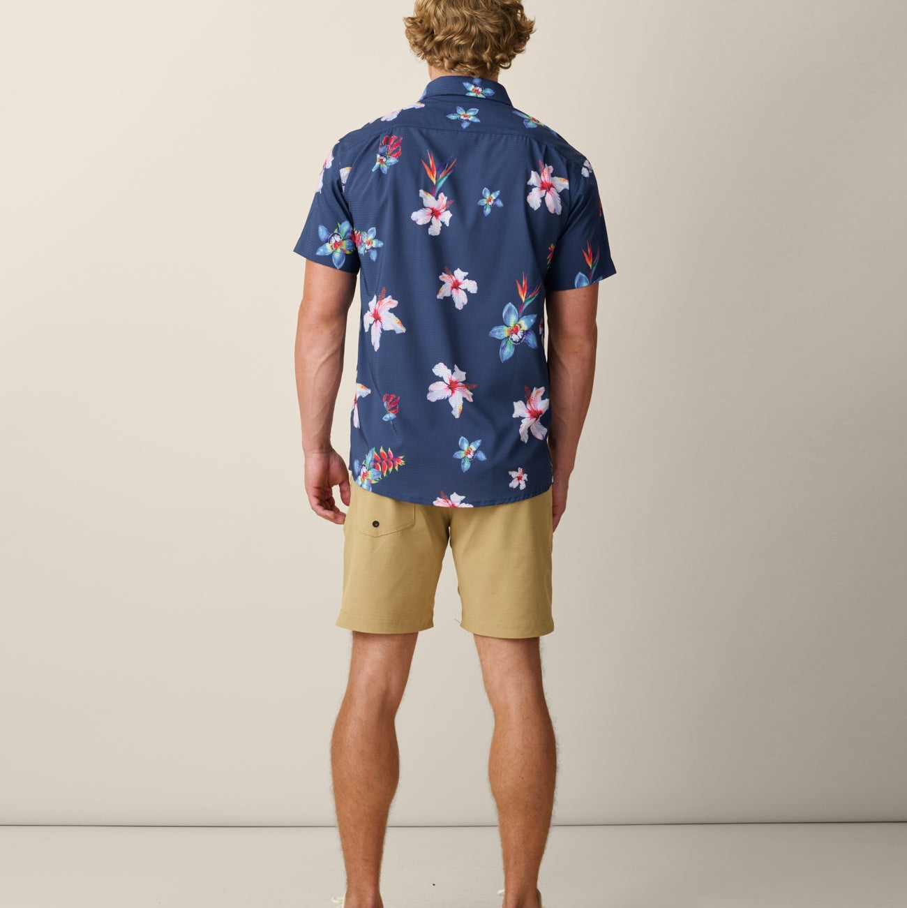 Man wearing a navy floral shirt and beige shorts on a plain background