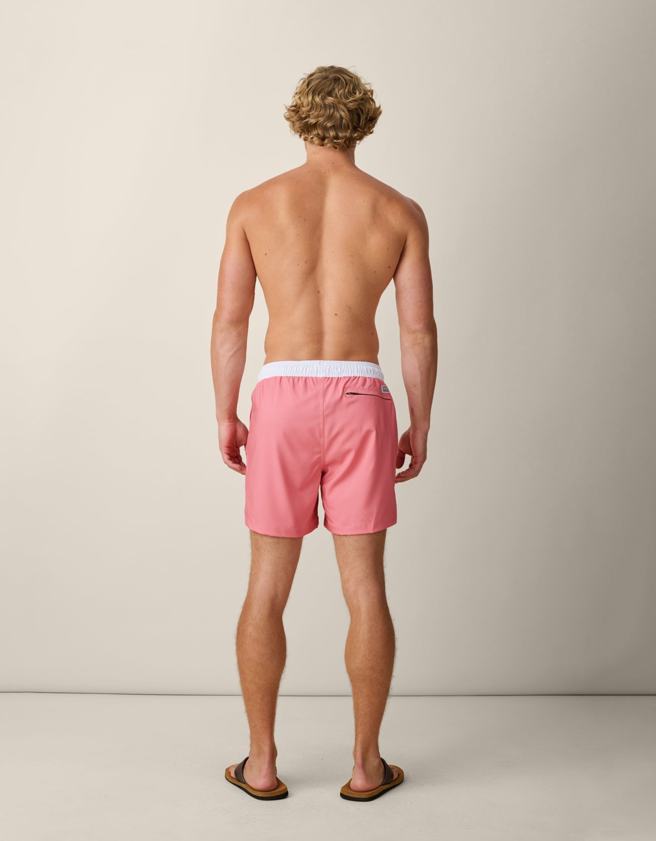 Man wearing pink swim shorts standing against a plain background