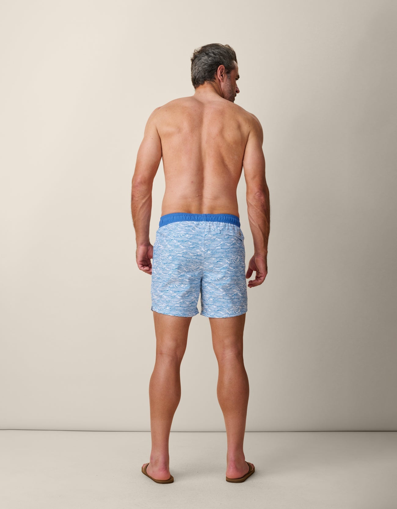 Man wearing blue swim shorts on a neutral background