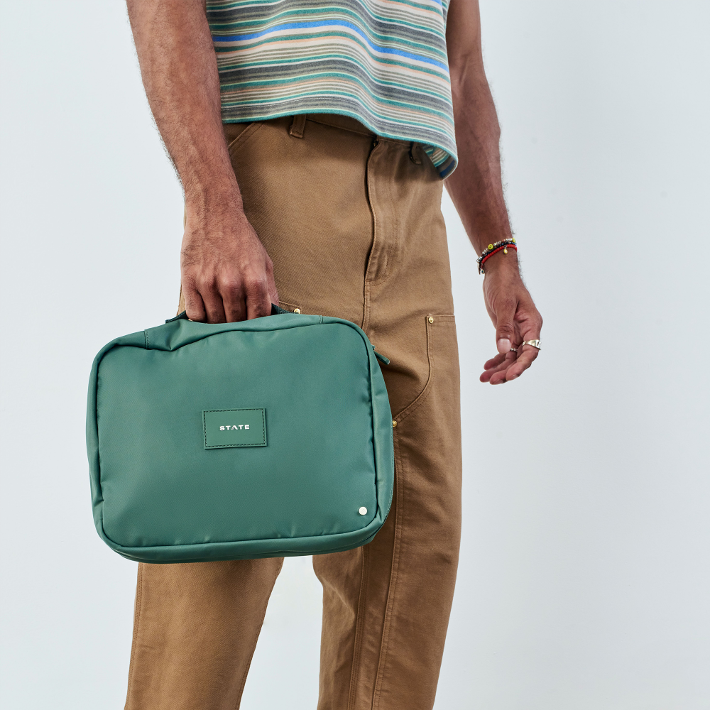 Person holding a green bag with a visible brand logo on a plain background