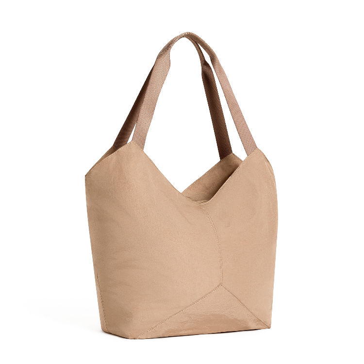 A minimalist slouchy tote bag in a warm tan or light brown color, shown from a three-quarter angle on a clean white background.