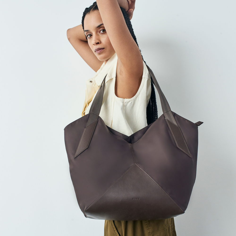 Woman holding a large brown leather tote bag against a plain background