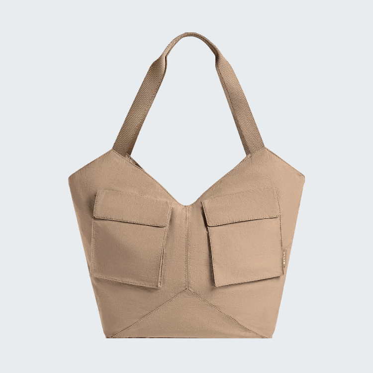 A structured beige shoulder bag with a unique geometric design, featuring two large front flap pockets and a single shoulder strap, shown against a plain white background.