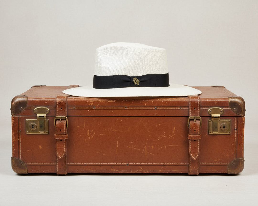 White Panama hat with a black band and gold emblem on a white background
