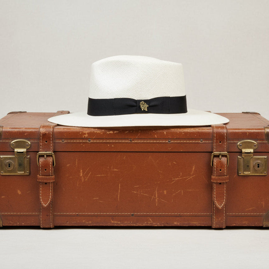 White Panama hat with a black band and gold emblem on a white background