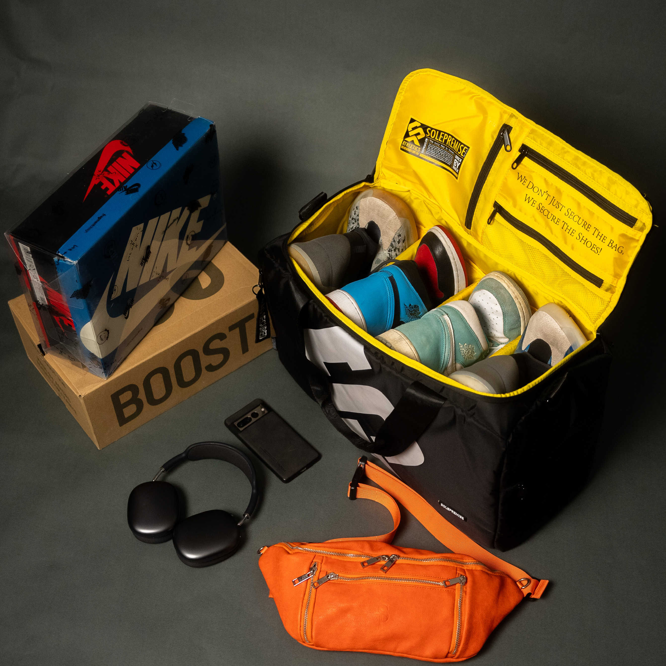 Open yellow bag with shoes, Nike box, phone, headphones, and orange bag on a dark surface