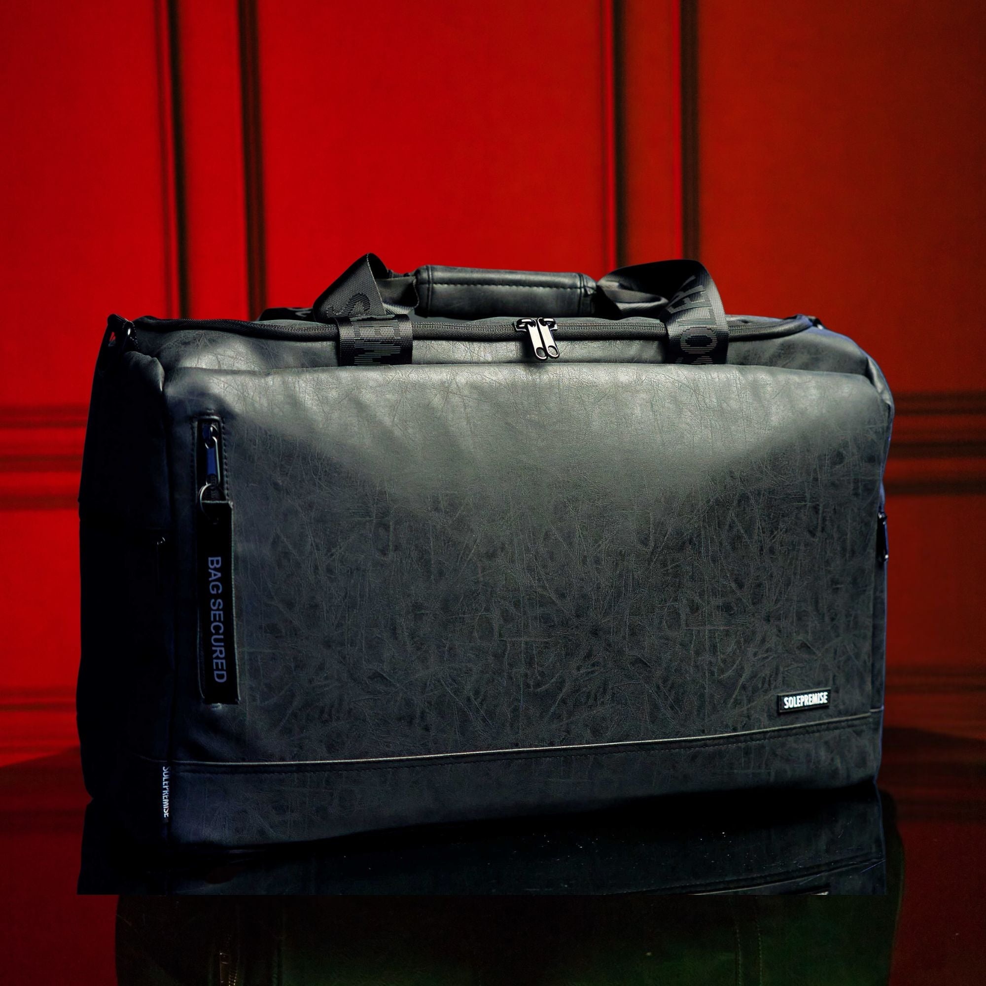 Gray duffel bag with geometric pattern on a reflective surface against a red background